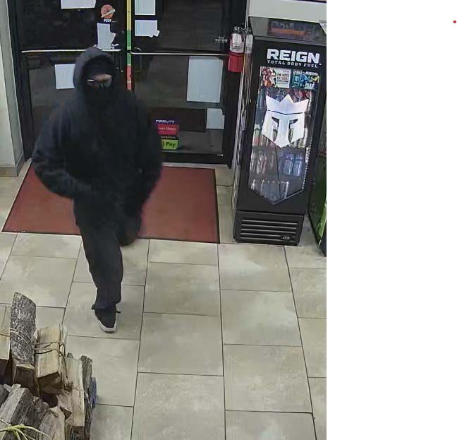 Camera footage photo of suspect dressed in all black, wearing glasses entering the gas station.